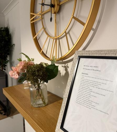 a vase of flowers on a table with a clock at 3 Stars Grètopp house in Little Hulton