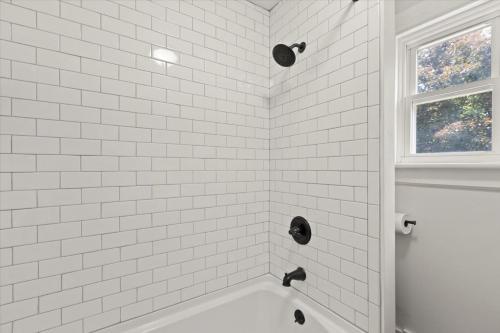 a white tiled bathroom with a tub and a window at Hudson Restored Farmhouse with Fire Pit in Hudson