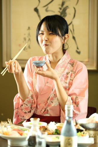 a woman sitting at a table eating food with chopsticks at Hotel Sunmi Club in Atami