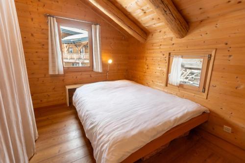 a bed in a wooden room with two windows at Chalet Dent d'Oche - A Dream Family Stay in Morgins