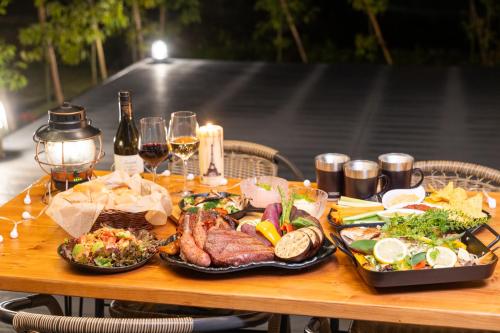 a wooden table topped with plates of food and wine at Relam Glamping Resort Gotemba in Gotemba