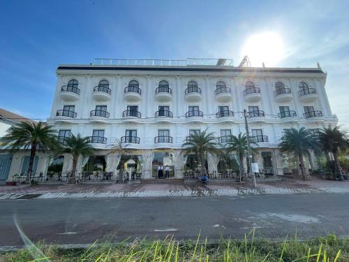 a large white building with palm trees in front of it at SUNRISE Hotel HA TIEN in Ha Tien