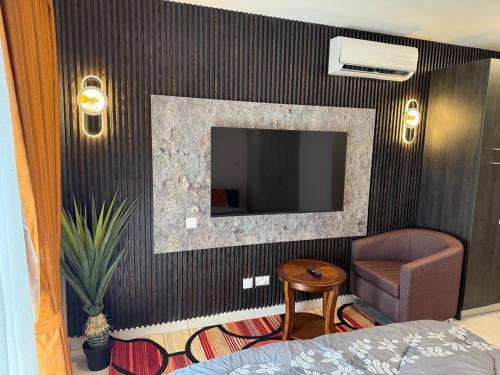 a bedroom with a tv on a wall with a chair at Loxwood Apartment Tetteh Quashie Accra Ghana in Accra