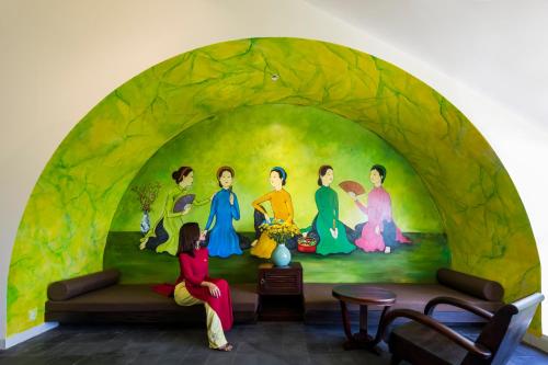 a woman sitting on a couch in front of a painting at Hoianoi Villa_A Little Hoi An_Entire villa in Hoi An