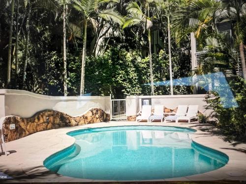 a swimming pool in a yard with chairs and trees at Carramah Noosa Heads apartment in Noosa Heads
