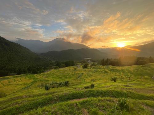 a sunset over a green field with mountains at ATASHIKADAYS Kumano-Kodo Beachfront B&B Hostel in Kumano