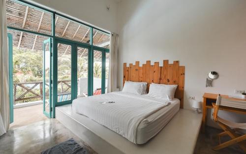 a bedroom with a bed and a desk and windows at Pajamas Koh Chang in Ko Chang