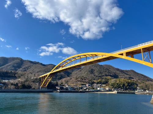 a yellow bridge over water with mountains in the background at La casa de Ikuchijima in Onomichi