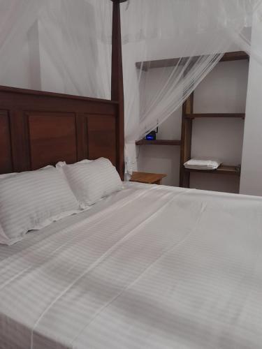a bedroom with a large white bed with a wooden headboard at Abraham Beach House in Tangalle
