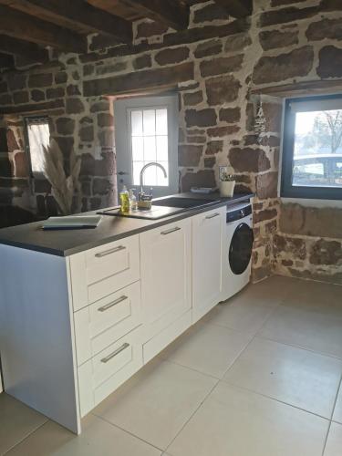 - une cuisine avec des placards blancs et un mur en pierre dans l'établissement Gite Le Fournil, à Saint-Pantaléon-de-Larche