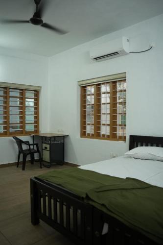 a bedroom with a bed and a desk and windows at RiverSoul Villa in North Paravur