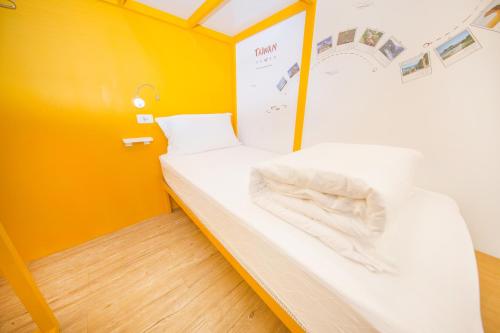 Cama pequeña en habitación con paredes amarillas en SleepBox Hostel en Taipéi