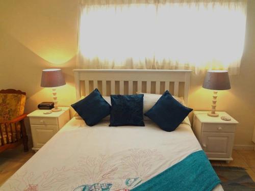 a bedroom with a bed with blue pillows and a window at Little Gem in Plettenberg Bay