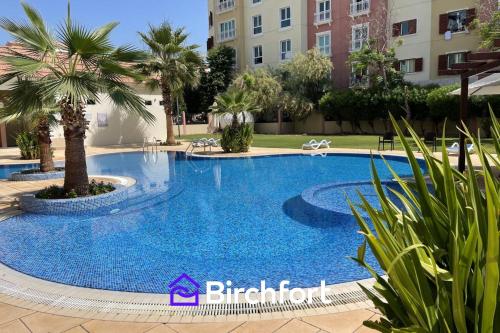 a large swimming pool with palm trees in a courtyard at Birchfort - Newly renovated unique 1 bedroom apartment in Dubai
