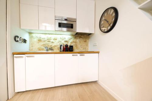 une cuisine avec des placards blancs et une horloge murale dans l'établissement CIA - Faubourg Montmartre Studio, à Paris