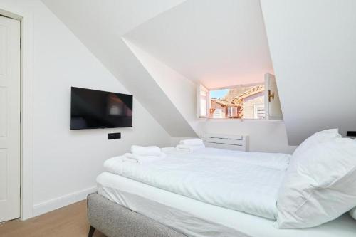 a white bedroom with a bed and a tv at Tudisi Loft Room in Dubrovnik