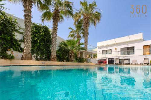 a swimming pool in front of a building with palm trees at Spacious 4BR Villa with Private pool, parking & BBQ by 360 Estates in Tal-Mirakli