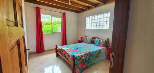 a room with a bed and a window with red curtains at Location Azuria Saint-Leu in Saint-Leu