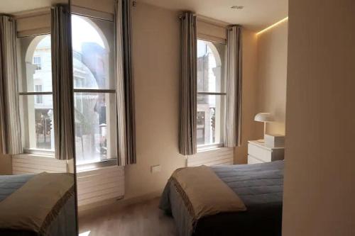 a bedroom with two beds and two large windows at 1 bedroom modern en-suite apartment Nine Elms in London