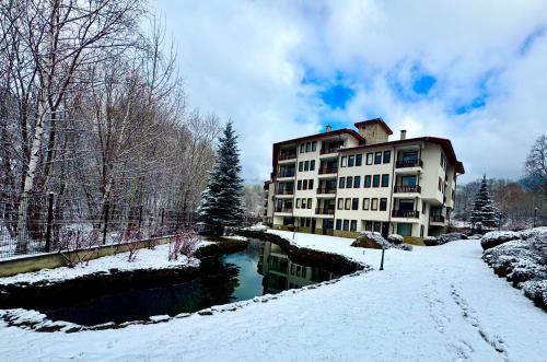 a building in the snow next to a river at Хубавото място - Ski & Relax next to Pamporovo in Smolyan