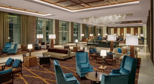 a hotel lobby with blue chairs and furniture and a chandelier at Kempinski Hotel Gold Coast City in Accra