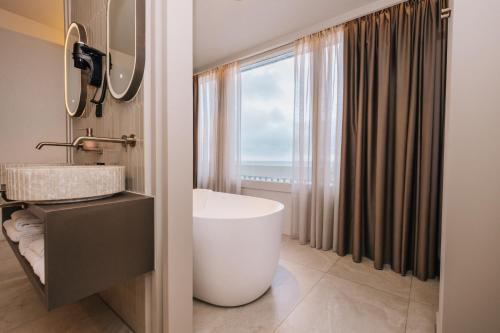 a bathroom with a large tub and a window at Palace Hotel Zandvoort in Zandvoort