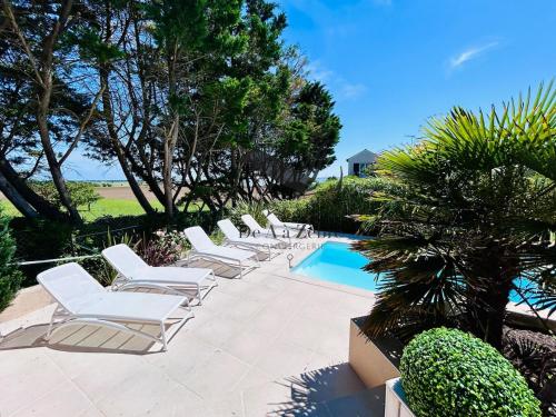 - une rangée de chaises longues blanches à côté de la piscine dans l'établissement Maison de Famille - Piscine chauffée et vue sur l'Océan Atlantique, à Le Port-des-Barques