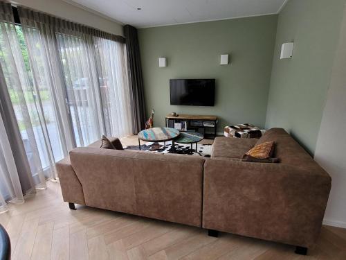 a living room with a brown couch and a flat screen tv at Villa Bosanemoon with Sauna | 6 persons in Gasselte