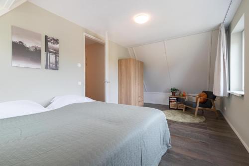a white bedroom with a bed and a chair at 't Boshuis Villa | 6 personen - Vakantiepark De Kremmer in Gasselte