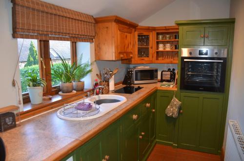 a kitchen with green cabinets and a sink at Green Farm Cottage in Ashbourne