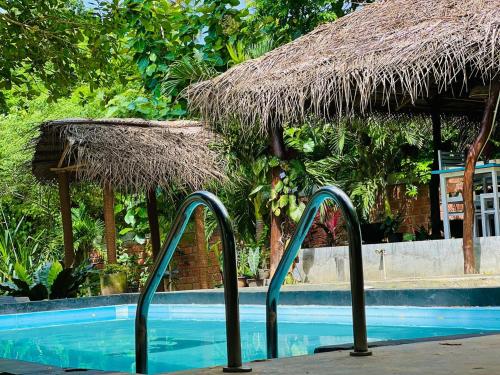 a swimming pool with a straw umbrella next to a swimming pool at Maritime Nest Cabanas in Tangalle