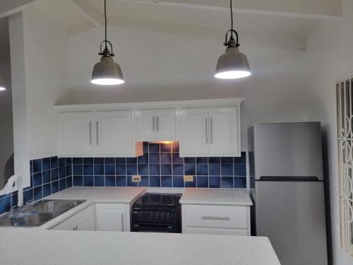 a kitchen with white cabinets and blue tiles on the wall at Swimming Pool- Balcony Veranda- Sea & Sunset Views in Dickenson Bay