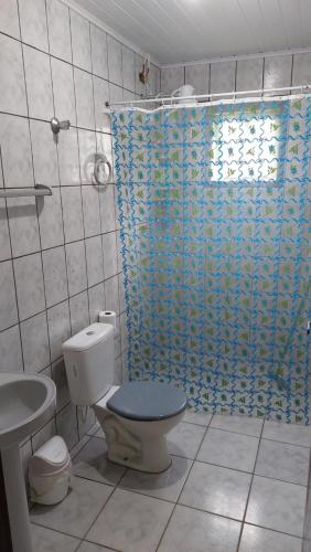 a bathroom with a toilet and a blue shower curtain at Maury Chalés Boiçucanga in São Sebastião
