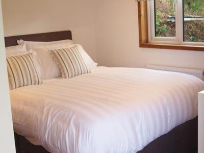 a white bed in a bedroom with a window at Longtails Lodge, near Bantham in Bantham