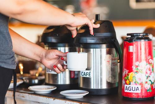 Eine Frau hält eine Kaffeetasse neben einer Kaffeemaschine. in der Unterkunft Hotel Atero in Sierra de la Ventana