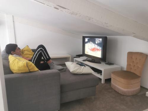 une femme assise sur un canapé en train de regarder une télévision dans l'établissement Appartement Gourette, à Eaux-Bonnes