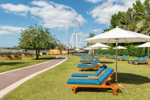 a row of lounge chairs and umbrellas in a park at Sheraton Jumeirah Beach Resort in Dubai