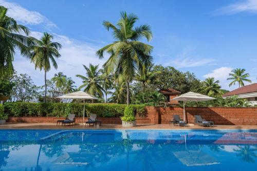 a swimming pool with chairs and umbrellas and palm trees at Fairfield by Marriott Goa Anjuna in Anjuna