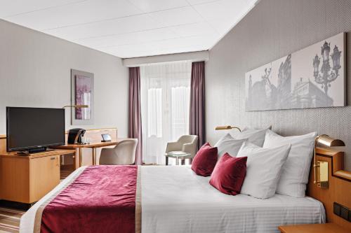 a hotel room with a bed with red and white pillows at Leonardo Royal Hotel Frankfurt in Frankfurt/Main