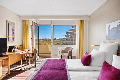 a hotel room with a bed and a desk and a window at Leonardo Royal Hotel Frankfurt in Frankfurt/Main