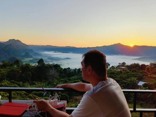 a man sitting on a balcony watching the sunset at บ้านชมหมอก ภูลังกา in Ban Sakoen