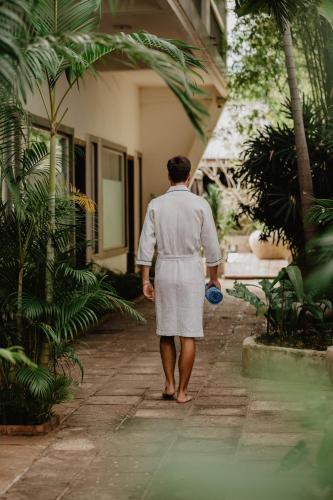 a man in a white uniform walking through a garden at La Bastide de Caro in Siem Reap