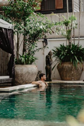 a man in a swimming pool next to plants at La Bastide de Caro in Siem Reap