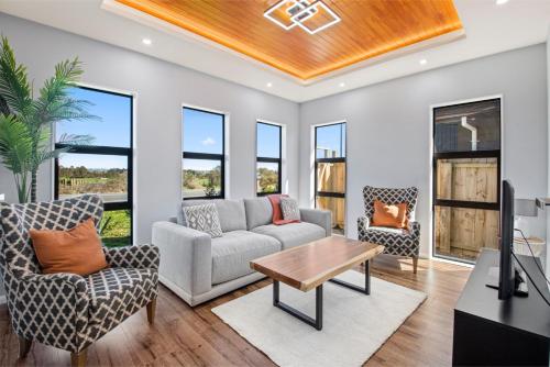 a living room with a couch and chairs and a tv at Beach Revival - Clarks Beach Holiday Home in Clarks Beach