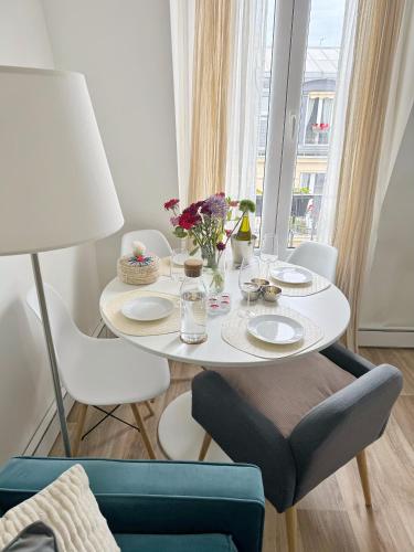 - une table blanche avec des assiettes et des fleurs dans une pièce dans l'établissement Appartement cosy au cœur du Paris 17eme, à Paris