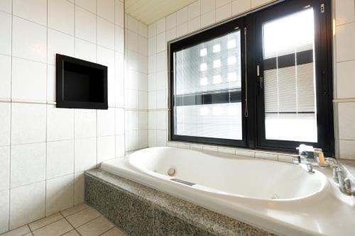 a bath tub in a bathroom with a window at Beppu Kanko Hotel Ace in Beppu