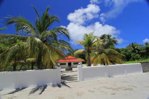 a house on the beach with palm trees and a white fence at Feridhoo Inn in Feridhoo