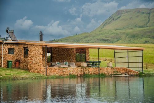 a stone house on the water next to a mountain at Mount Lake Cabins in Harrismith