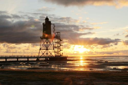 a lighthouse on the beach with the sunset in the background at Ferienhaus Nordkönig mit Sauna und Whirlpool in Langen