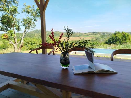 a wooden table with a book and a vase with flowers at Roukh Kiri Khaoyai, The Centara Collection in Pak Chong